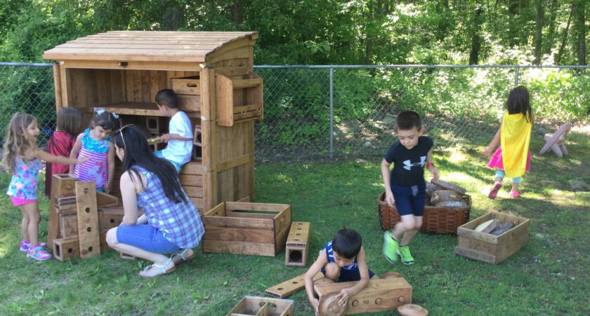 Kids outside building a car out of wood blocks.